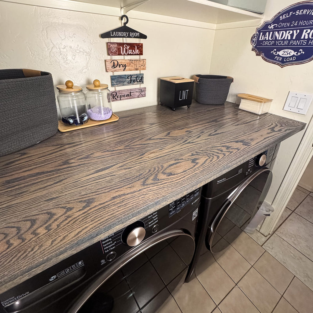 Dark oak laundry room countertop installed over front load washer and dryer with storage and decor