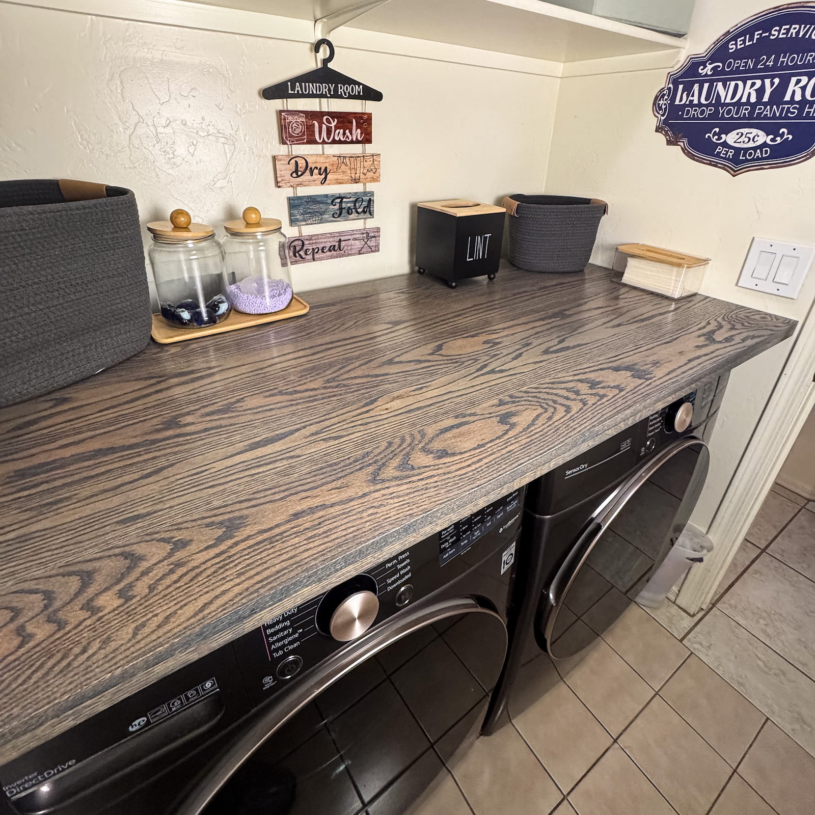 Dark oak laundry room countertop installed over front load washer and dryer with storage and decor