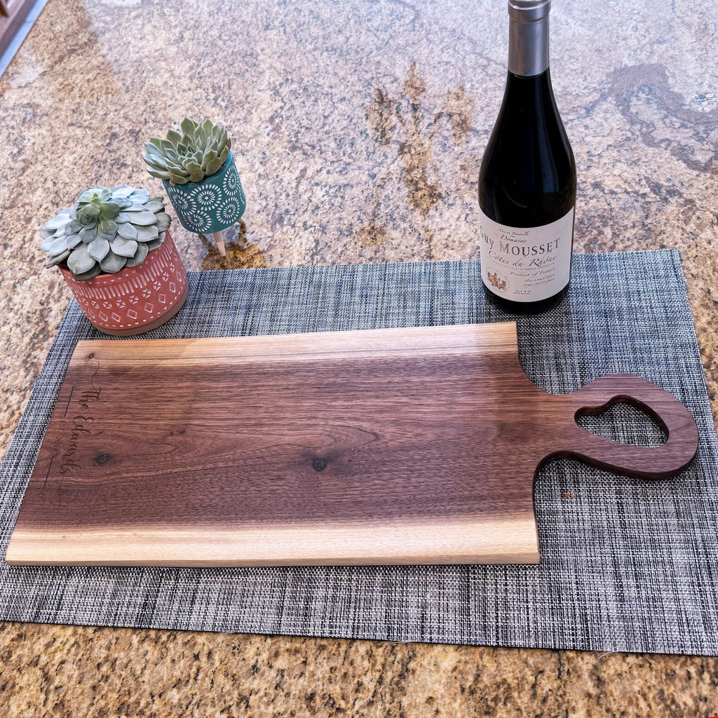Live edge walnut charcuterie board with heart-shaped handle beside wine bottle