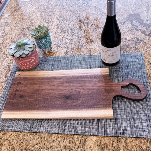 Live edge walnut charcuterie board with heart-shaped handle beside wine bottle