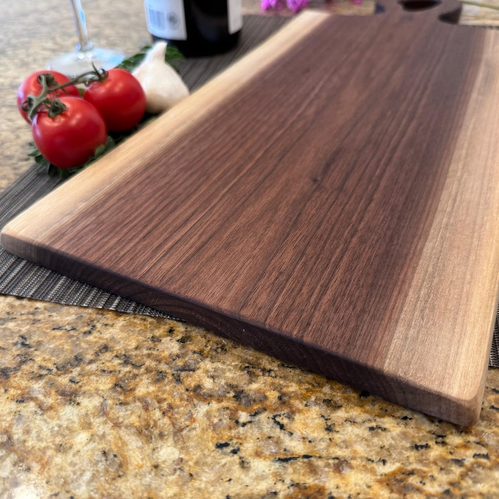 Handmade walnut live edge charcuterie board on kitchen countertop with tomatoes and garlic