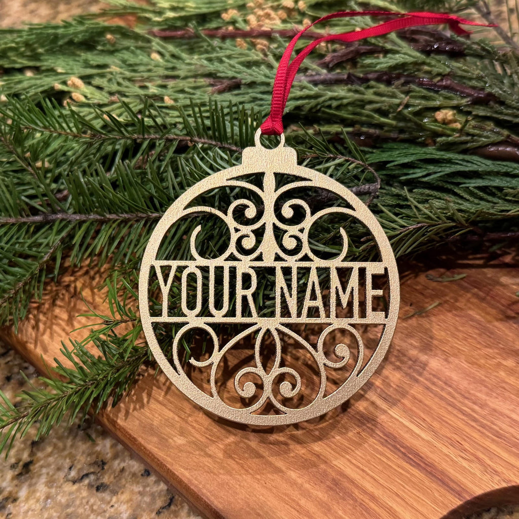 Personalized glitter gold Christmas ornament with custom name and red ribbon on evergreen branches
