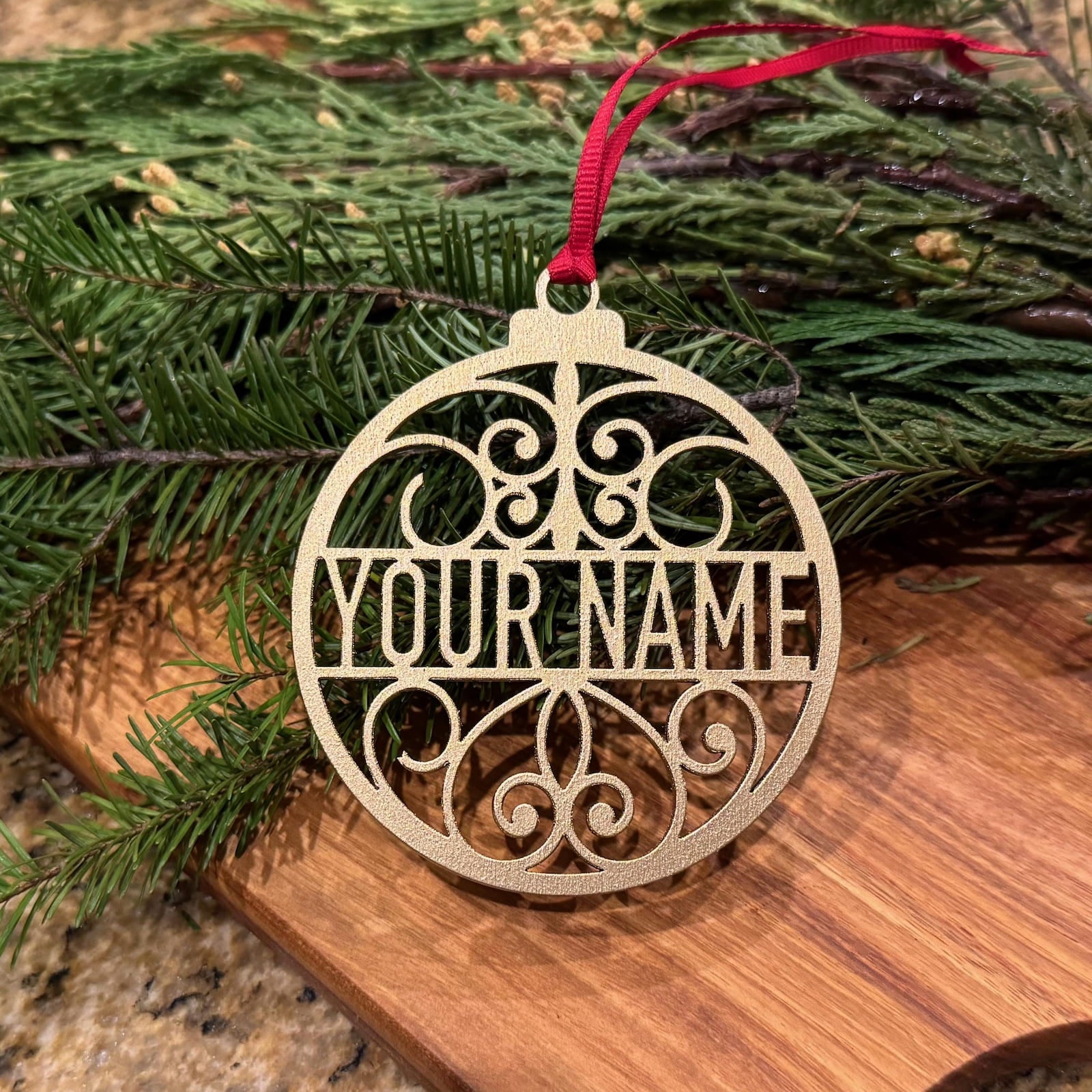 Personalized glitter gold Christmas ornament with custom name and red ribbon on evergreen branches