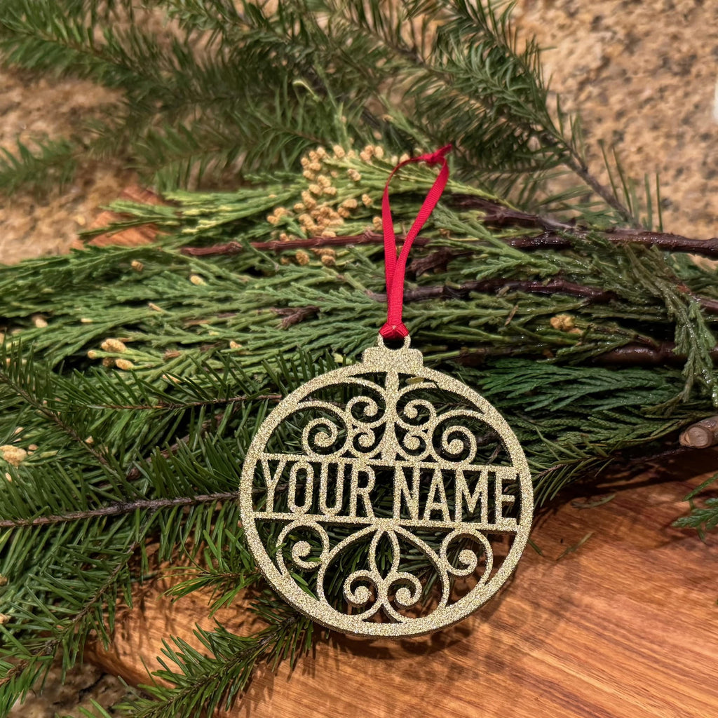 Personalized glitter gold Christmas ornament with custom name and red ribbon on evergreen branches