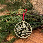 Personalized glitter gold Christmas ornament with custom name and red ribbon on evergreen branches