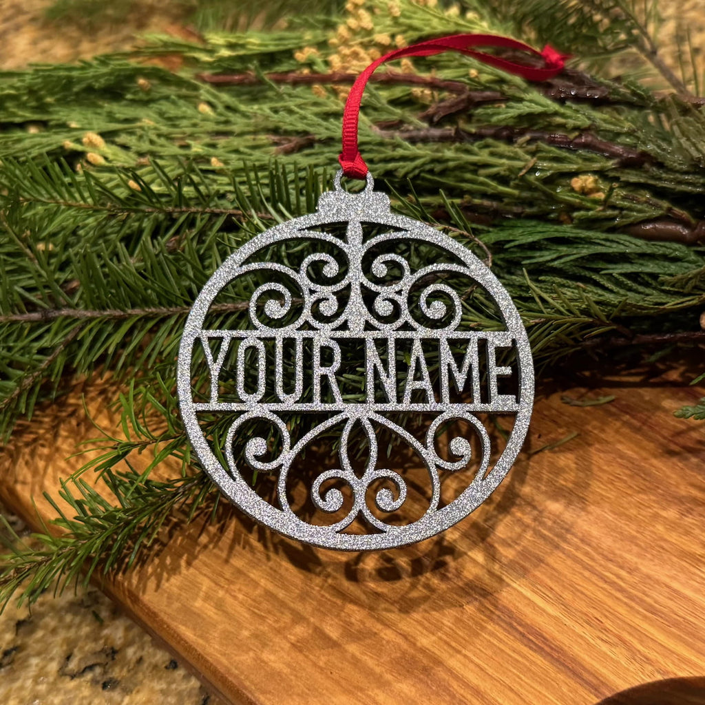 Personalized glitter silver Christmas ornament with custom name and red ribbon on evergreen branches