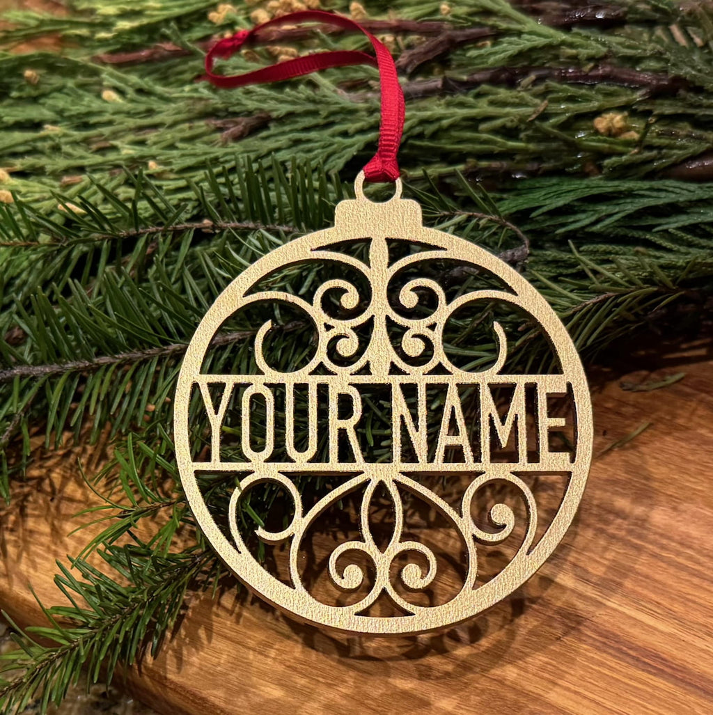 Personalized metallic gold Christmas ornament with custom name design displayed on evergreen branches