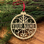 Personalized metallic gold Christmas ornament with custom name design displayed on evergreen branches