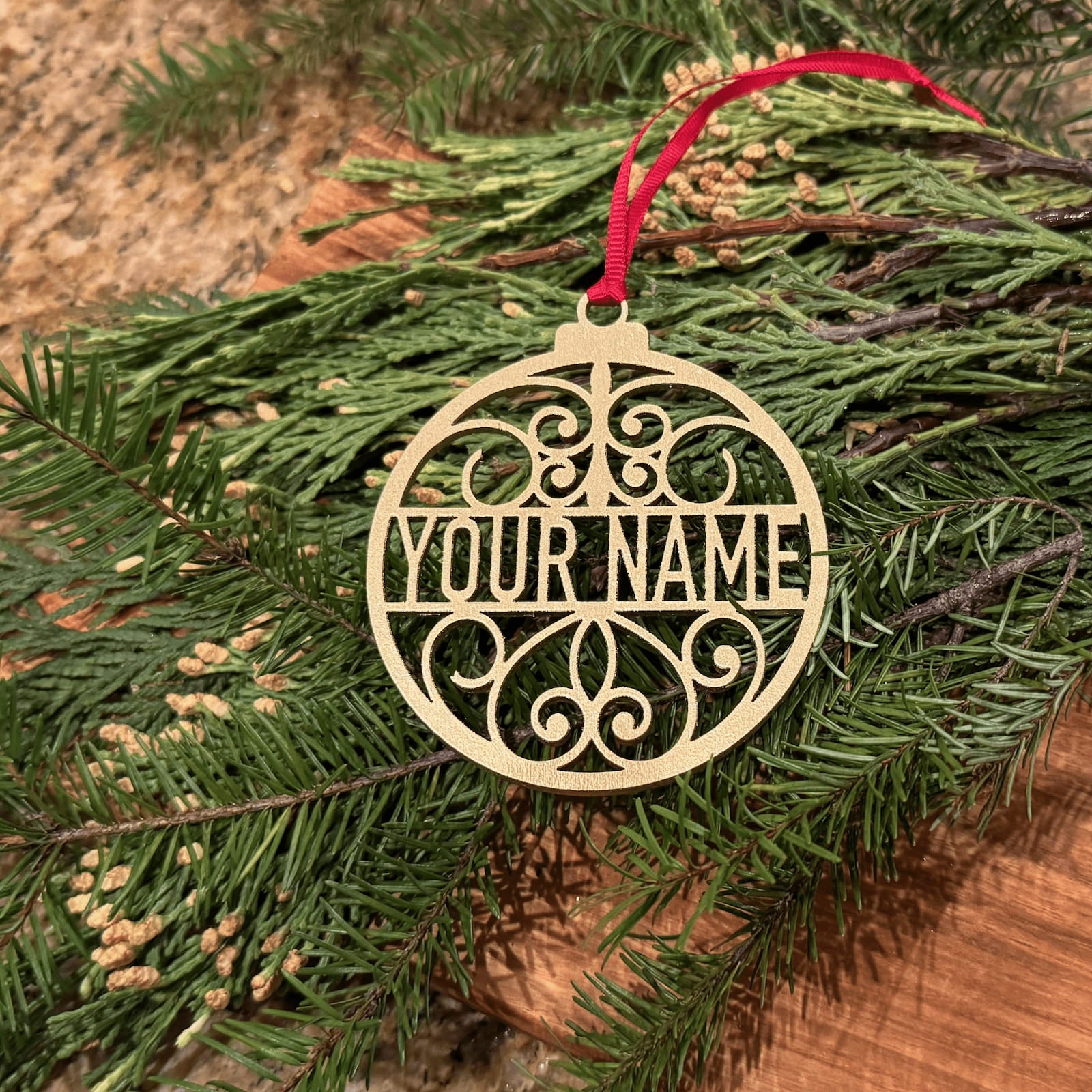 Personalized metallic gold Christmas ornament with custom name and red ribbon on evergreen branches
