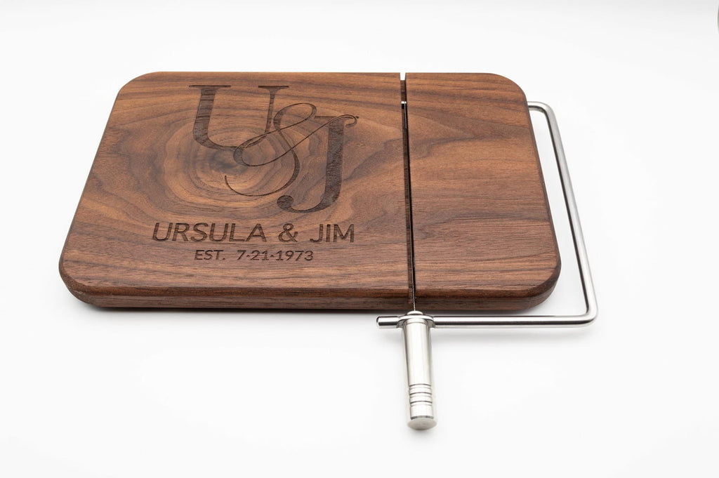 Personalized walnut cheese slicer engraved with couples monogram, names, and wedding date on a white background