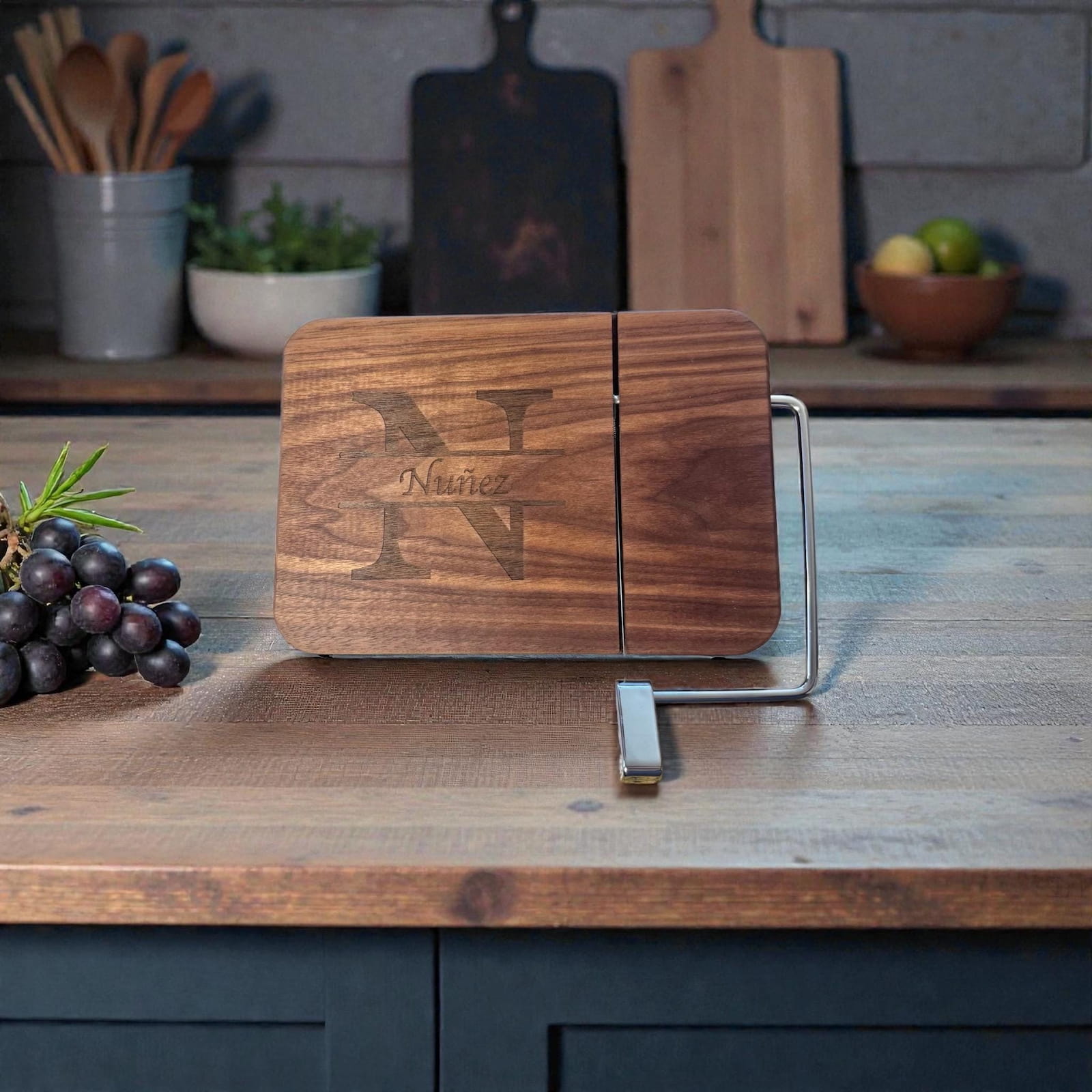 Personalized walnut cheese slicer with split monogram engraving displayed on a kitchen countertop with grapes