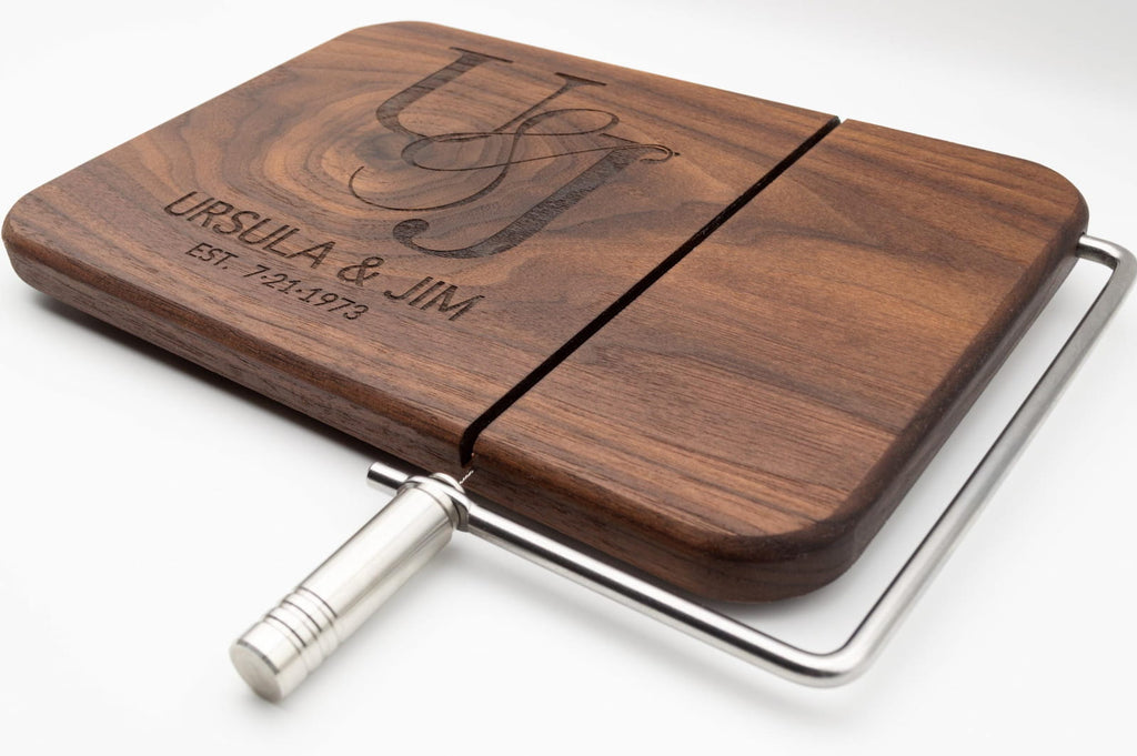 Personalized walnut cheese slicer with engraved couples monogram, names, and anniversary date on a white background
