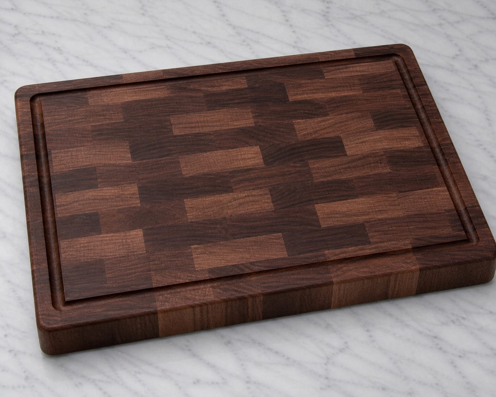 Plain walnut end grain cutting board with juice groove on marble background