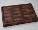 Plain walnut end grain cutting board with juice groove on marble background